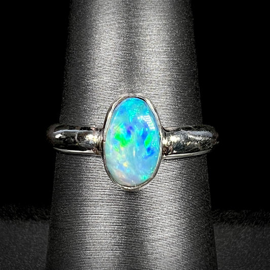 A women's pure silver Australian opal solitaire ring with blue and green colors shown close-up on a ring display against a black background.