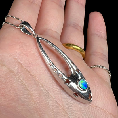 A sterling silver and opal doublet ballerina shoe necklace shown close-up from an angle in a hand.