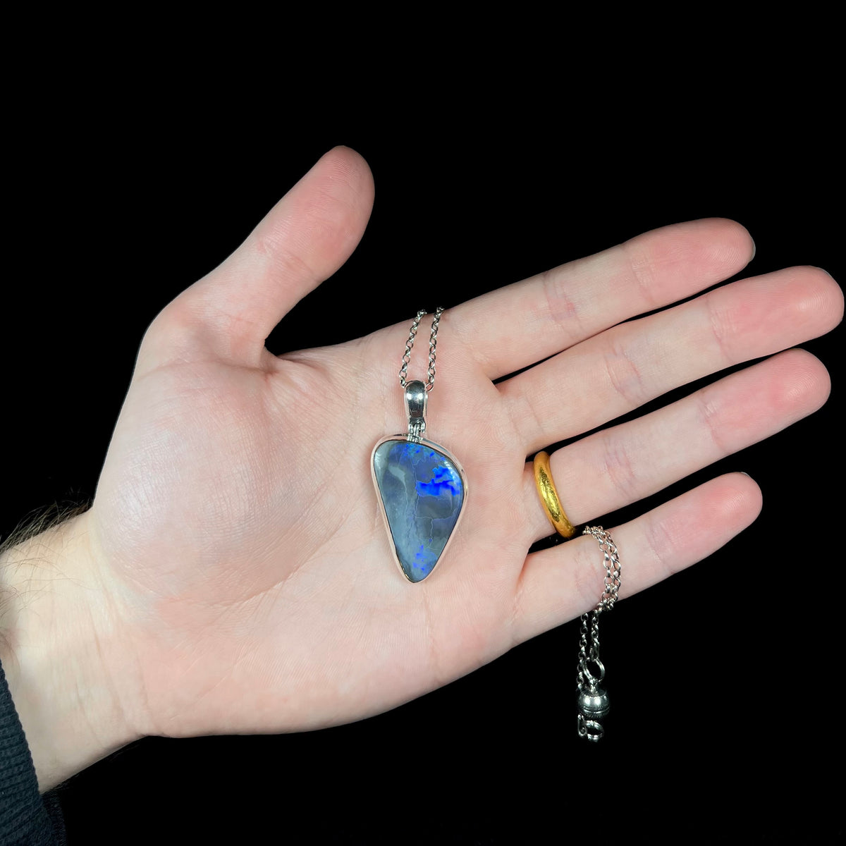 Hand holding sterling silver black opal necklace with silver chain