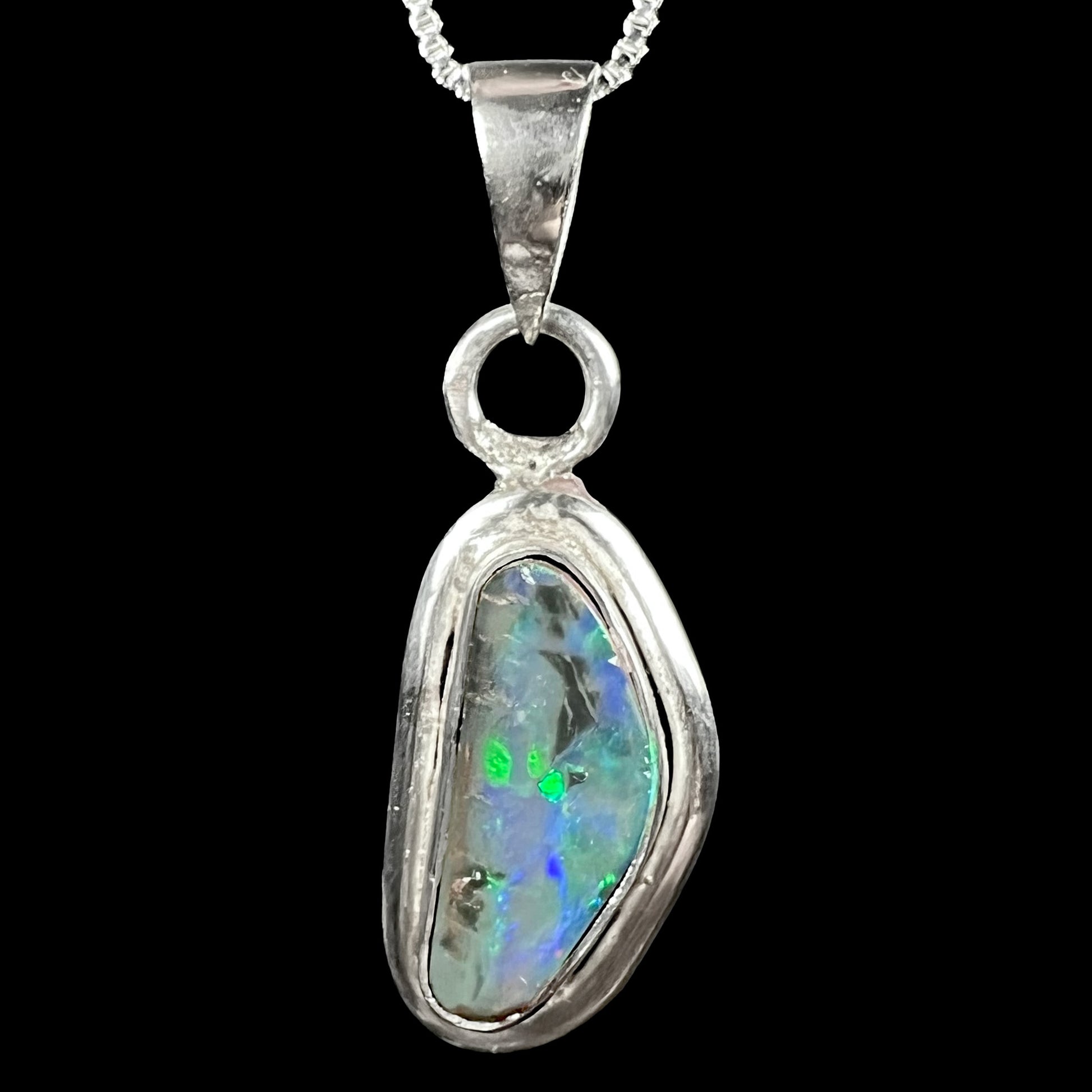 Front close-up of a unisex sterling silver Australian black opal pendant with green and blue flashes, shown on chain against black background.