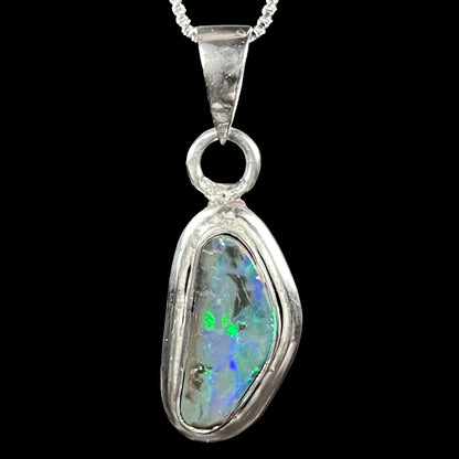 Front close-up of a unisex sterling silver Australian black opal pendant with green and blue flashes, shown on chain against black background.