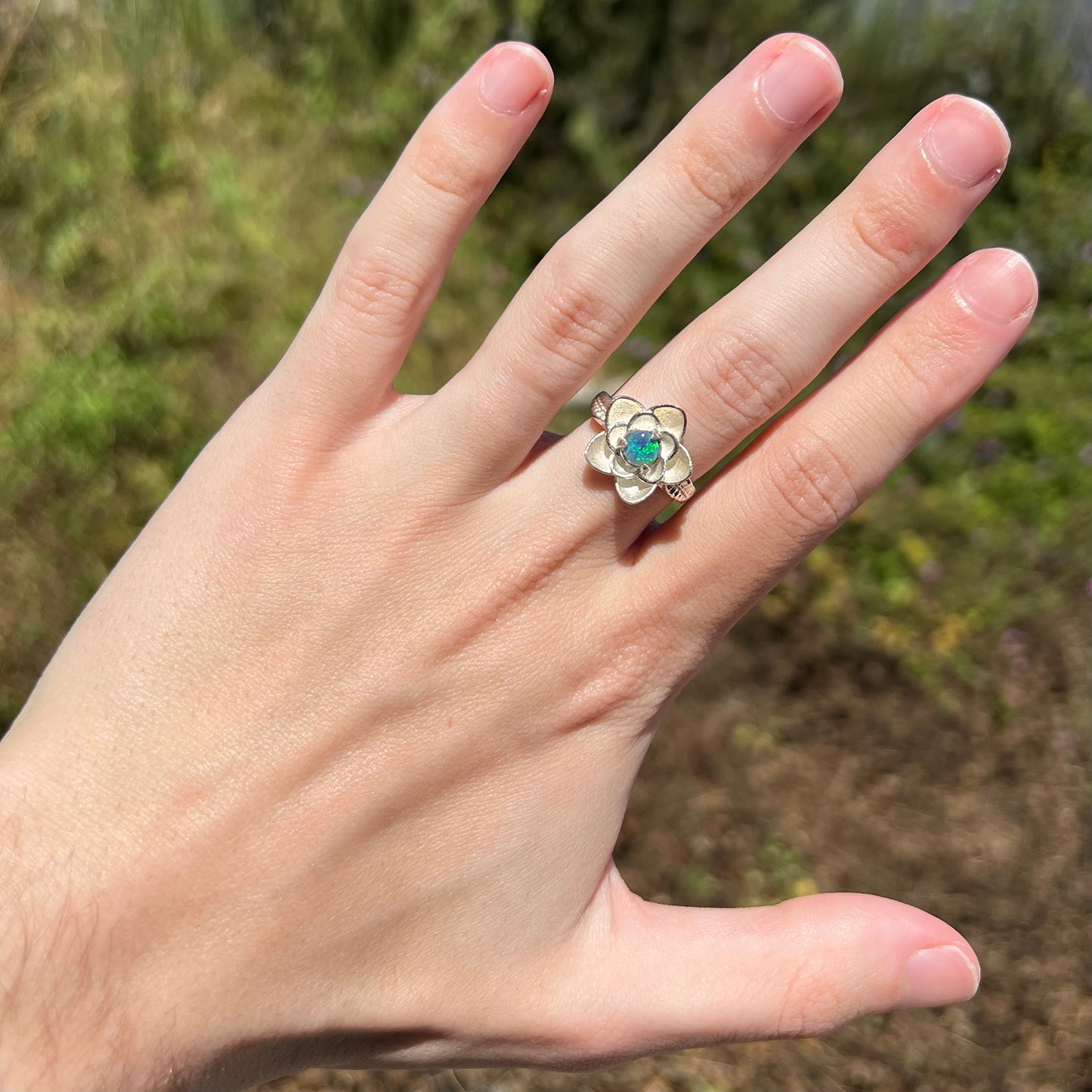Hand in sunlight wearing women's sterling silver black opal ring with lotus flower design