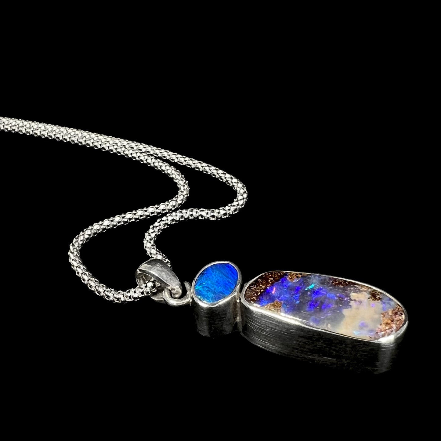 A stylish angled shot of a handmade sterling silver boulder opal necklace, highlighting its deep blue opal and natural ironstone matrix.