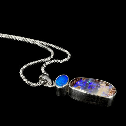 A stylish angled shot of a handmade sterling silver boulder opal necklace, highlighting its deep blue opal and natural ironstone matrix.