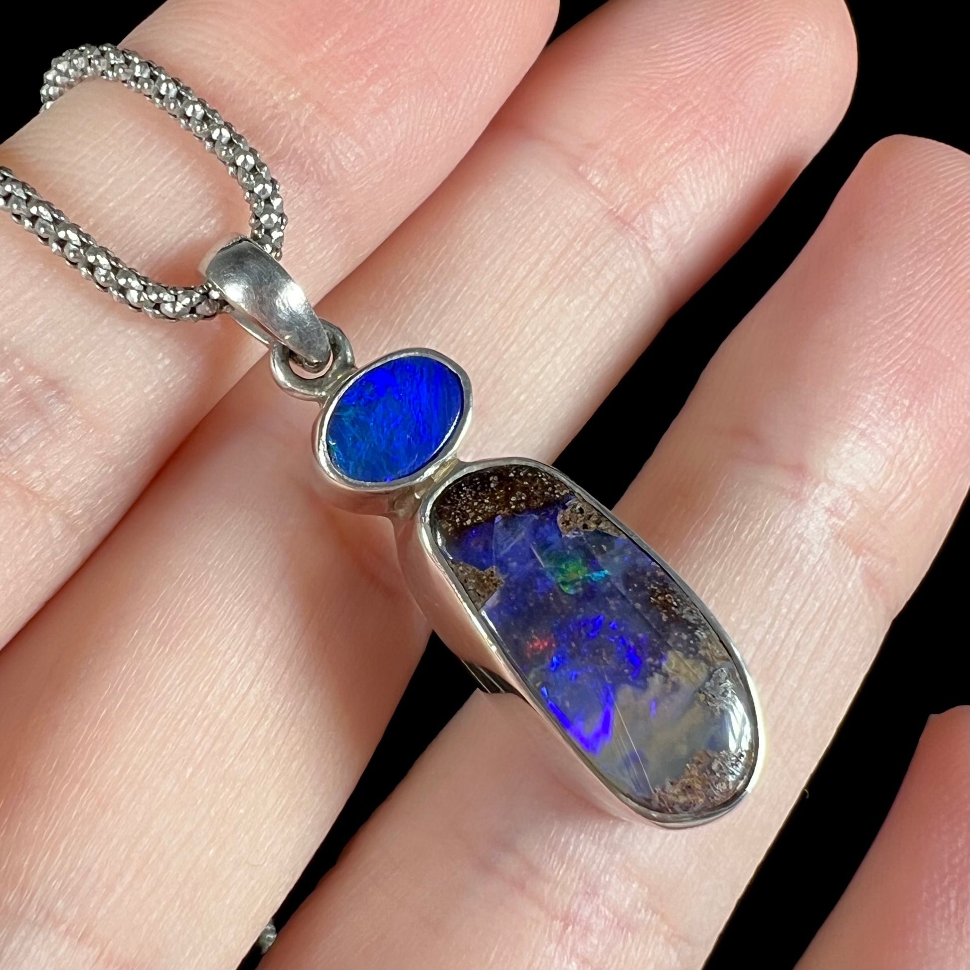 An angled macro shot of a sterling silver boulder opal necklace, showing a mix of faint red, green, and blue flashes in LED lighting.