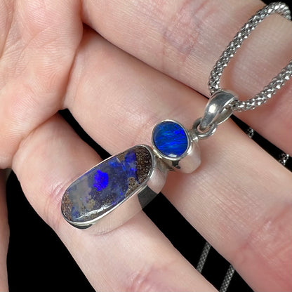 A macro close-up of the side view of a sterling silver boulder opal necklace, displaying only blue opal fire in its deep body tone.