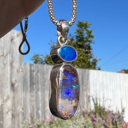 A macro close-up of a sterling silver boulder opal necklace in natural sunlight, revealing blue opal flashes from a twisted angle.