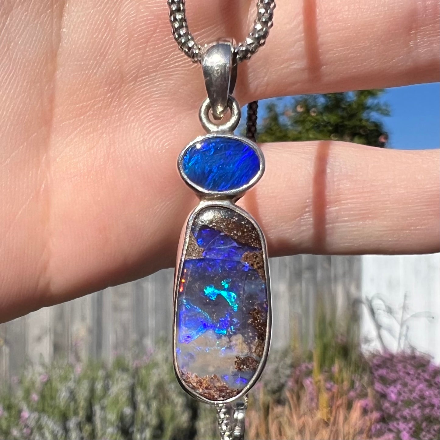 A macro shot of a sterling silver boulder opal necklace in natural sunlight, displaying a greenish-blue opal flash.