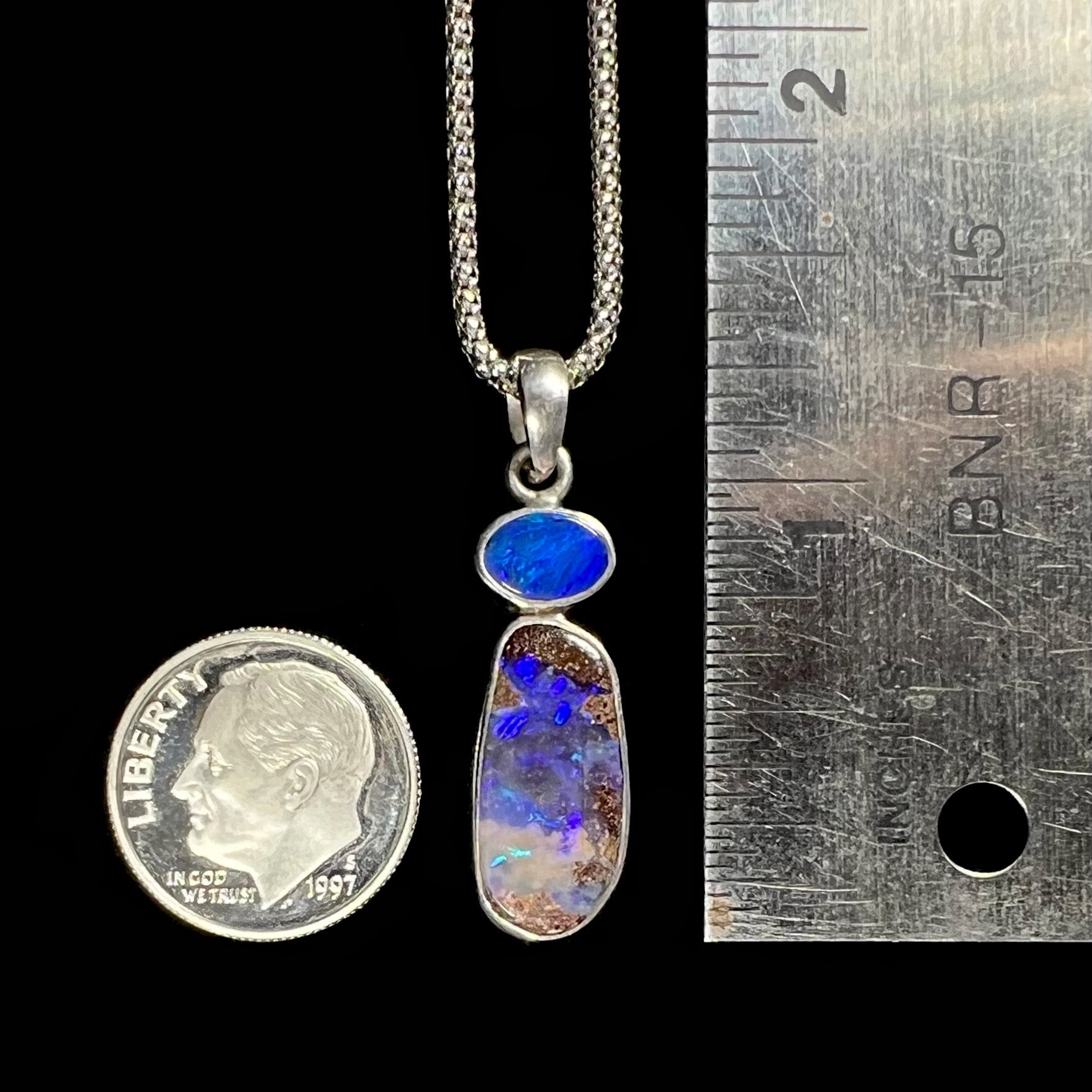 A sterling silver boulder opal necklace placed next to a dime and ruler for scale, showing its 1.25-inch pendant size.