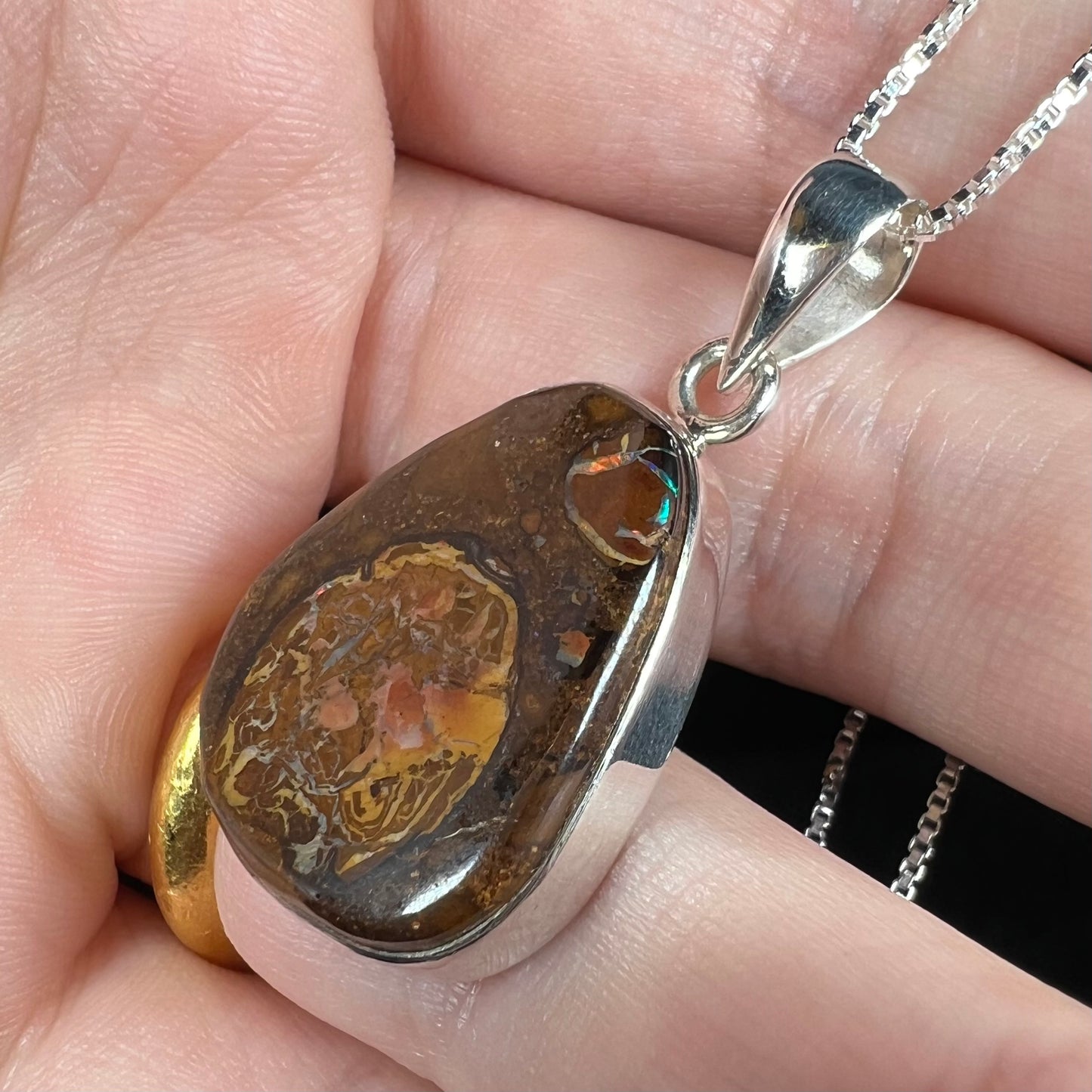 Angled view of a Yowah nut boulder opal pendant in sterling silver, shown close-up in a hand.
