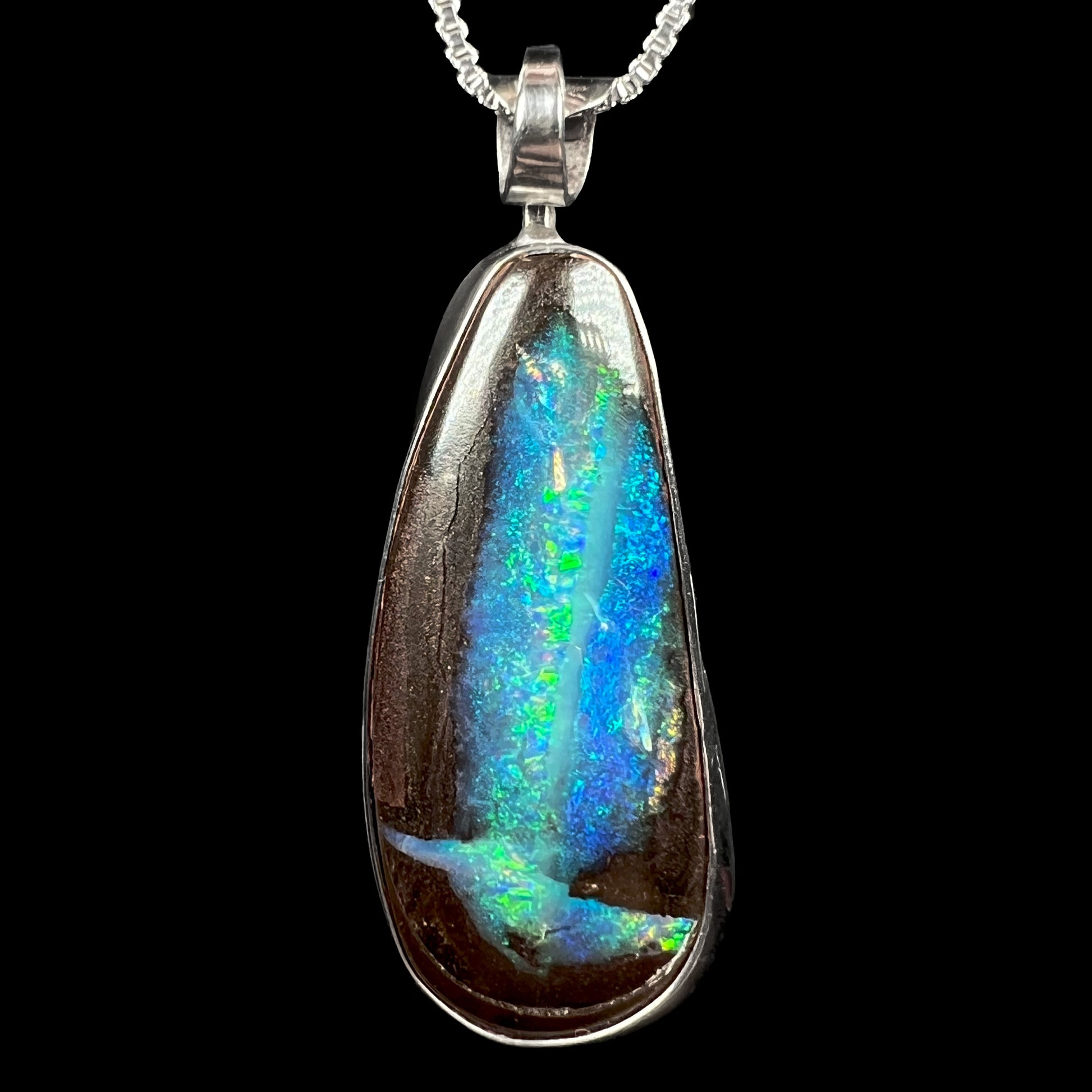 A sterling silver boulder opal pendant with glittering blue and green color play, shown against a black background.