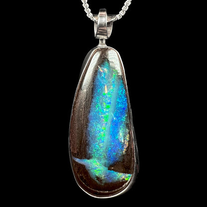 A sterling silver boulder opal pendant with glittering blue and green color play, shown against a black background.