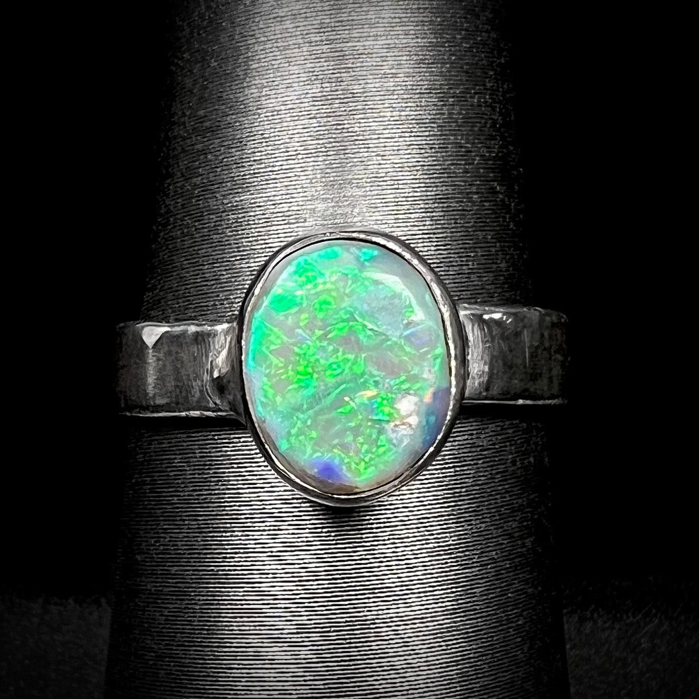 A unisex .999 fine silver Lightning Ridge opal solitaire ring with a bright green flash of color, shown close-up on a ring display against black background.