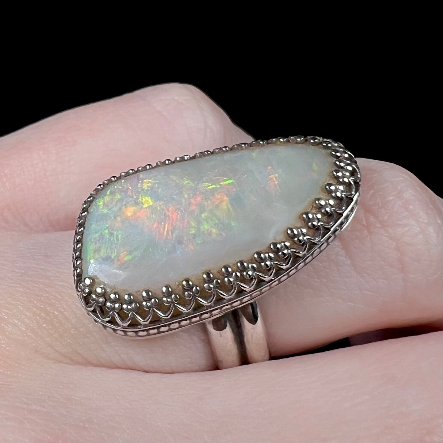 Close-up of a sterling silver Australian opal ring with a crown design worn on a hand and shown from an angle.