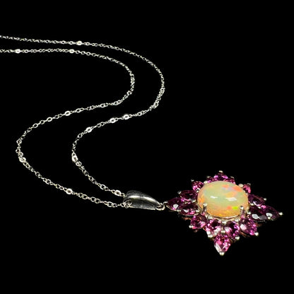 A sterling silver Ethiopian opal and rhodolite garnet spray necklace shown from angle laying on black backdrop.