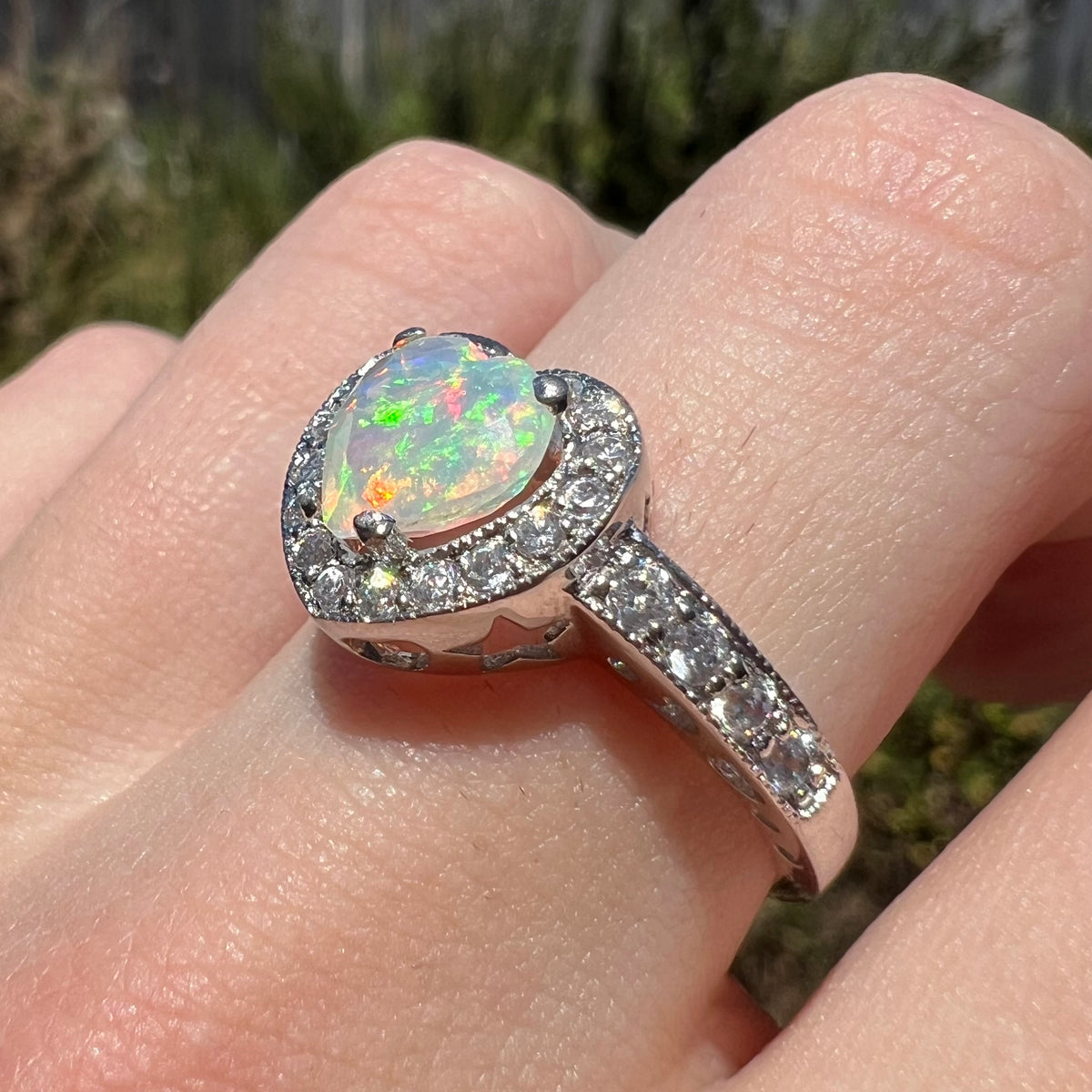 Sterling silver Ethiopian opal heart ring with CZ accents and halo design, worn on a finger in sunlight, viewed from close-up angle
