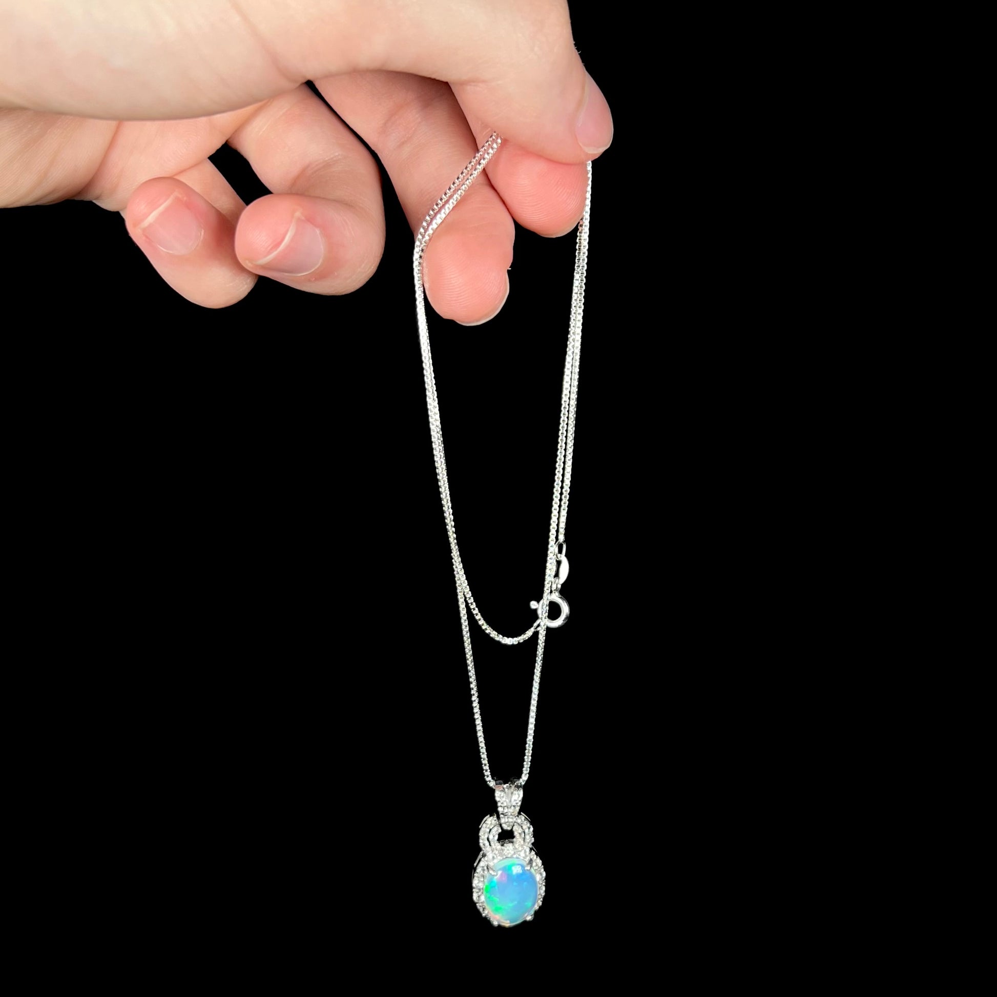 Hand dangling sterling silver Ethiopian opal and white topaz halo necklace from chain