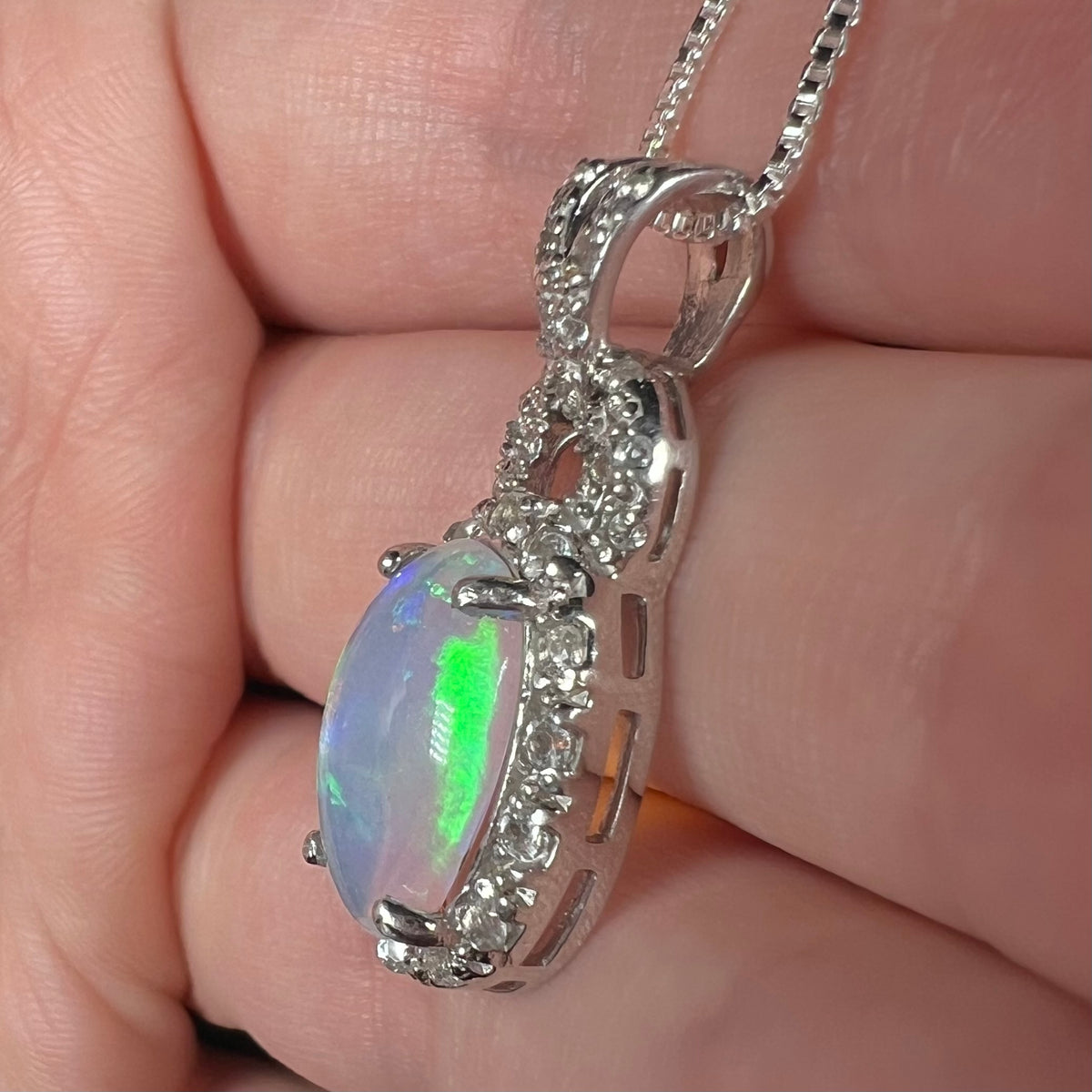 Side view of sterling silver Ethiopian opal and topaz halo pendant, held in hand