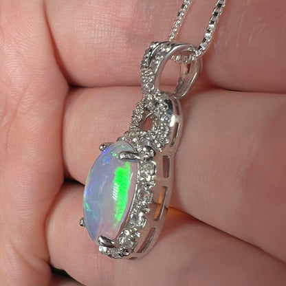 Side view of sterling silver Ethiopian opal and topaz halo pendant, held in hand