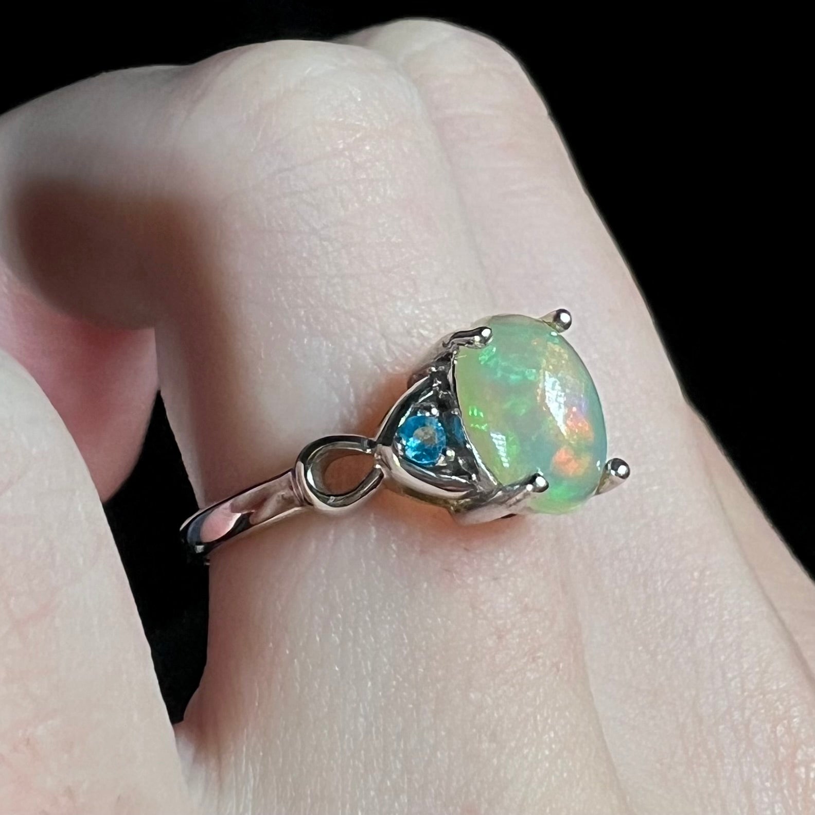 Angled view of sterling silver Ethiopian opal ring with blue apatite accents on finger