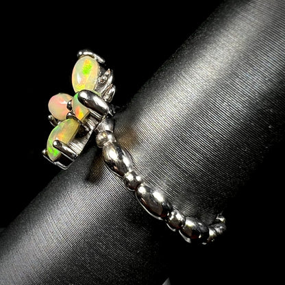 Side view of a sterling silver Ethiopian opal butterfly ring, shown on a ring display.  The shank has a rounded design.