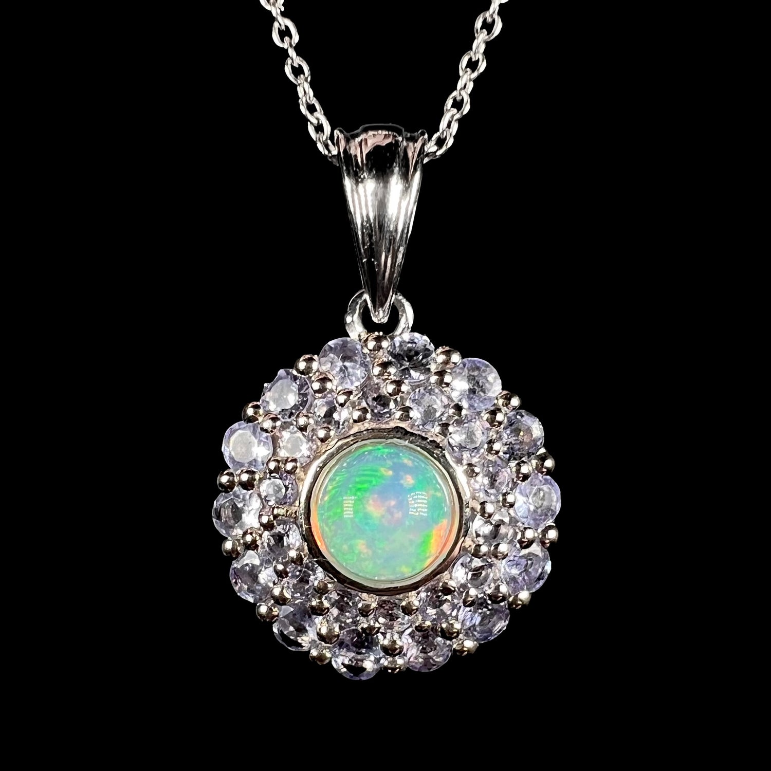 Front close-up of a sterling silver women's pendant set with a round Ethiopian fire opal in the middle of a double halo of light denim blue tanzanites, shown on a silver chain.