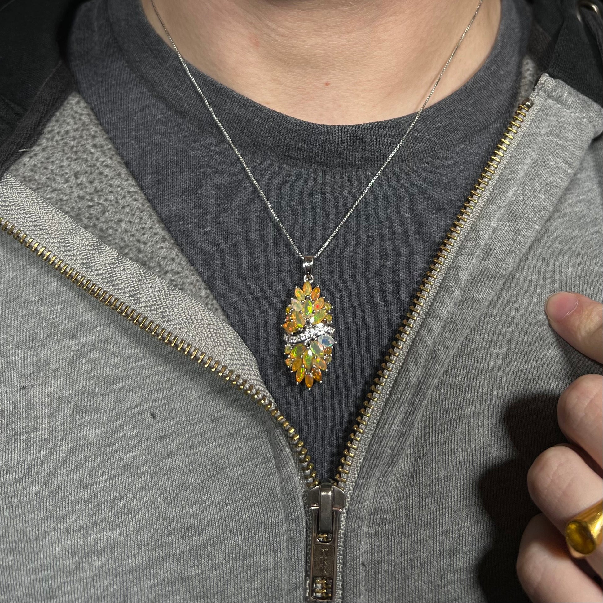 Close-up of a person's neck and chest area wearing a sterling silver Ethiopian opal cluster necklace with white zircon accents against a dark shirt beneath a hoodie.