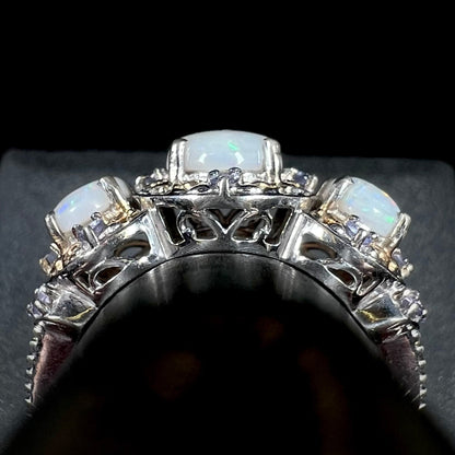 Side gallery profile view of filigree details on the basket of a sterling silver three-stone opal and tanzanite ring, shown on a ring display.