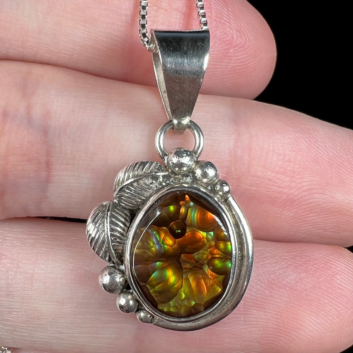 Macro view of sterling silver fire agate pendant with Southwest leaf and bead design, held in hand.