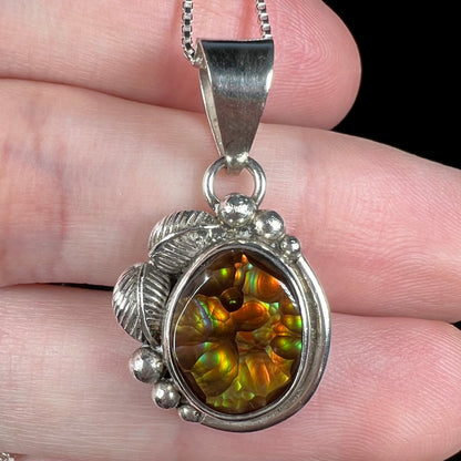 Macro view of sterling silver fire agate pendant with Southwest leaf and bead design, held in hand.
