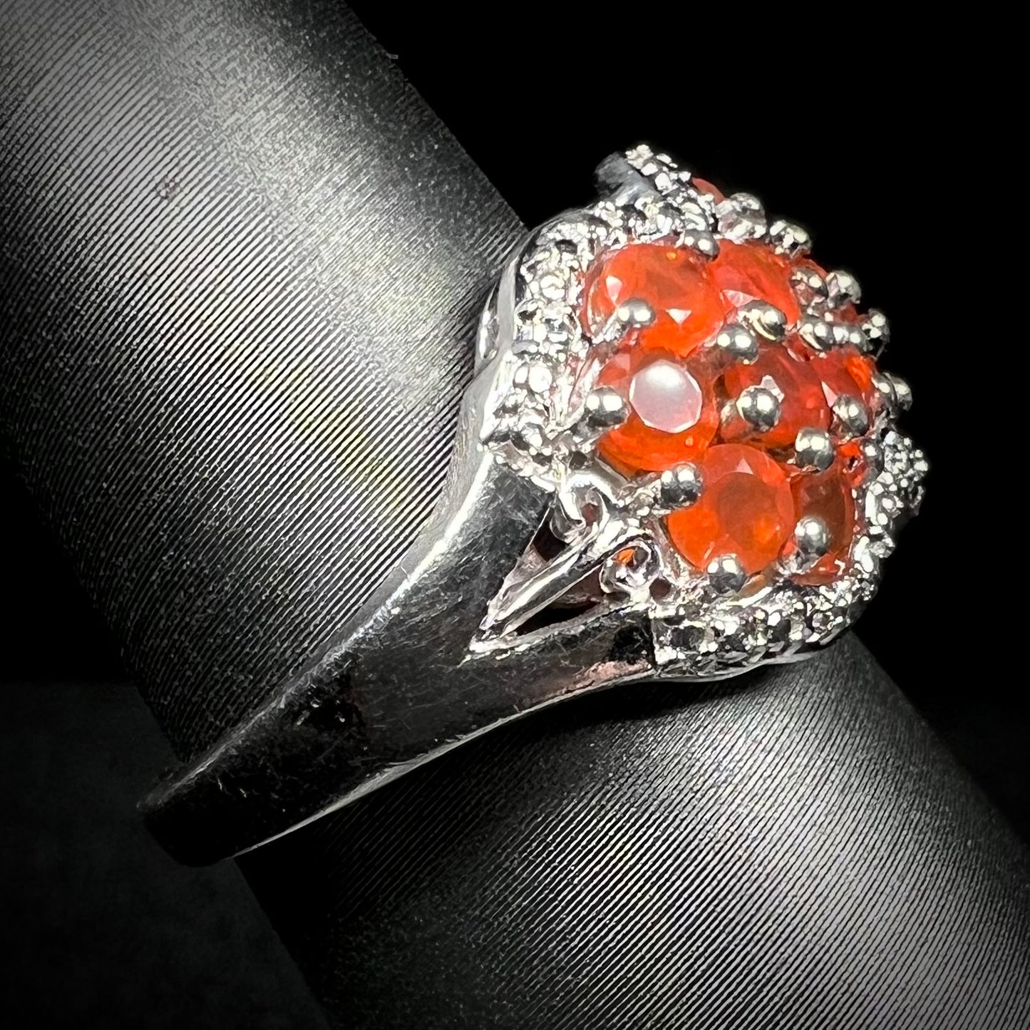 Side close-up of a sterling silver fire opal ring on a ring display, focused on the ring's shank and a filigree accent. 