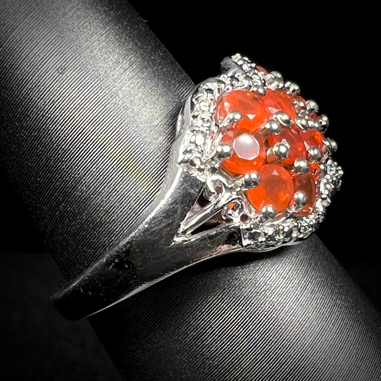 Side close-up of a sterling silver fire opal ring on a ring display, focused on the ring's shank and a filigree accent. 
