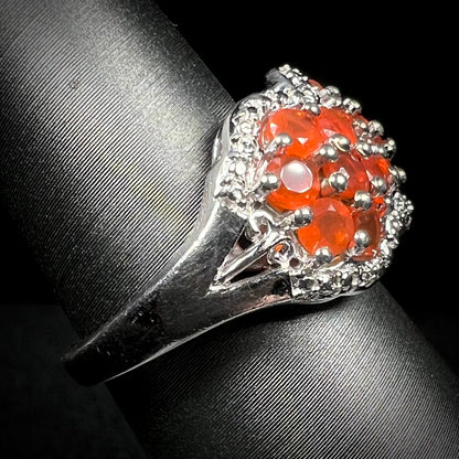 Side close-up of a sterling silver fire opal ring on a ring display, focused on the ring's shank and a filigree accent. 
