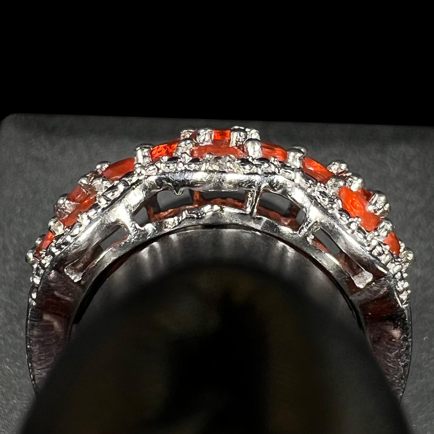 Side gallery profile view of a sterling silver fire opal ring on a ring display.  Part of the gallery is missing a piece, a defect from casting.