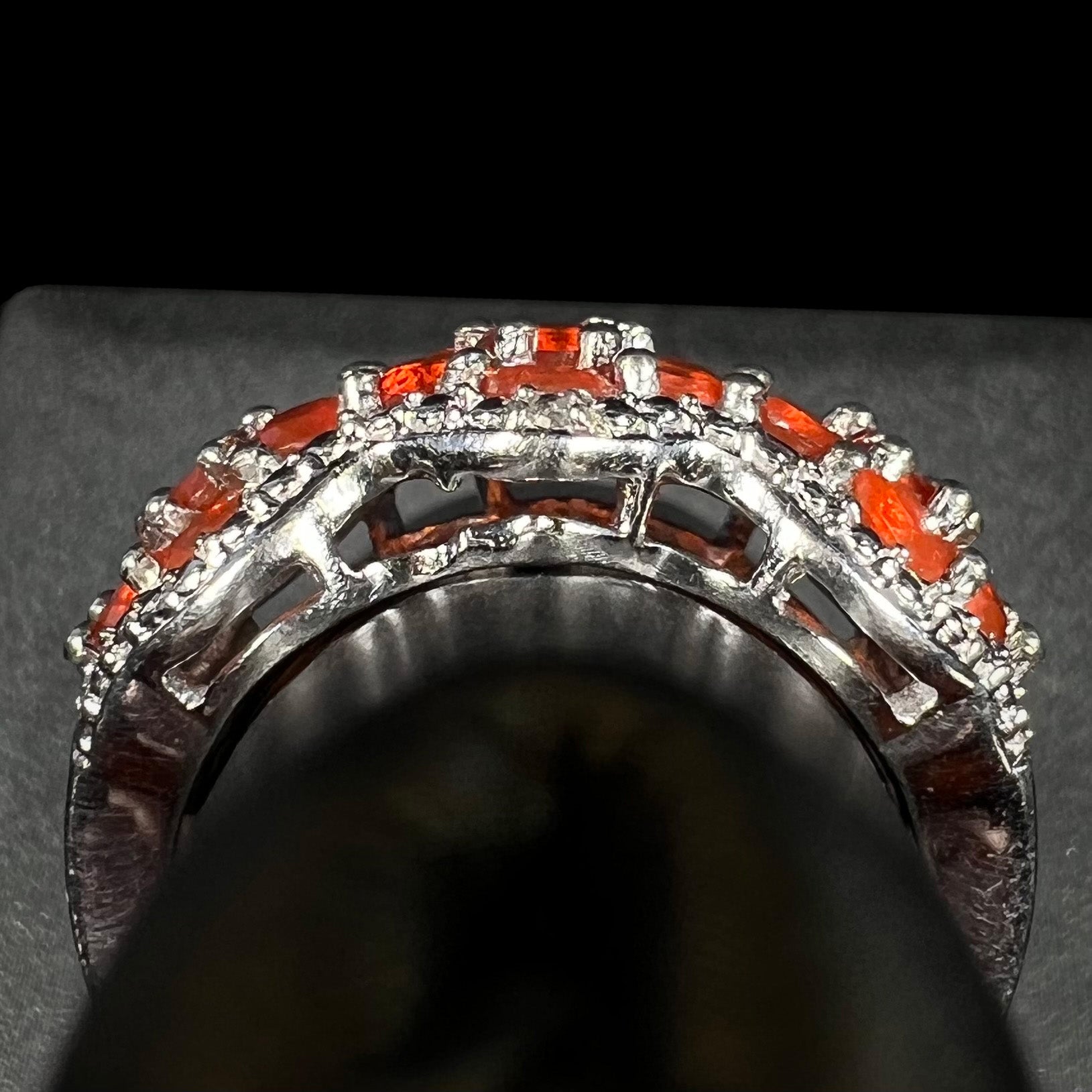 Side gallery profile view of a sterling silver fire opal ring on a ring display.  Part of the gallery is missing a piece, a defect from casting.