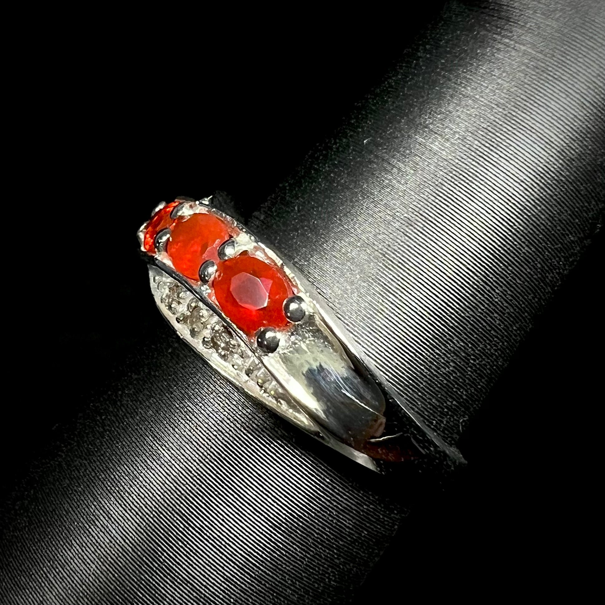 Side view of Mexican fire opal and diamond ring in sterling silver against a black background.  Ring's shank in focus.