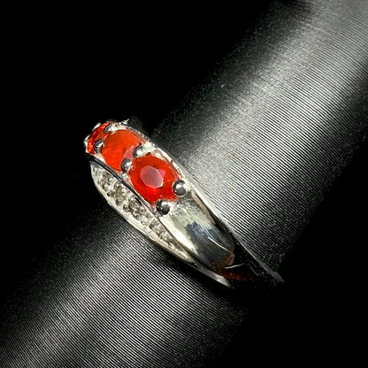 Side view of Mexican fire opal and diamond ring in sterling silver against a black background.  Ring's shank in focus.