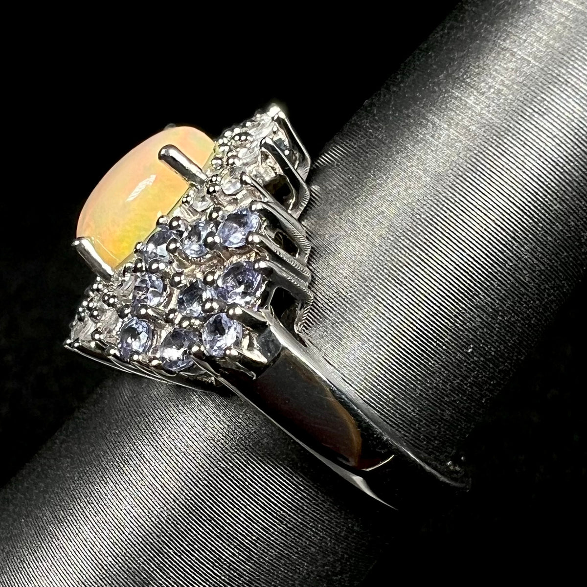 Side view of sterling silver fire opal ring with tanzanite accents, on ring display