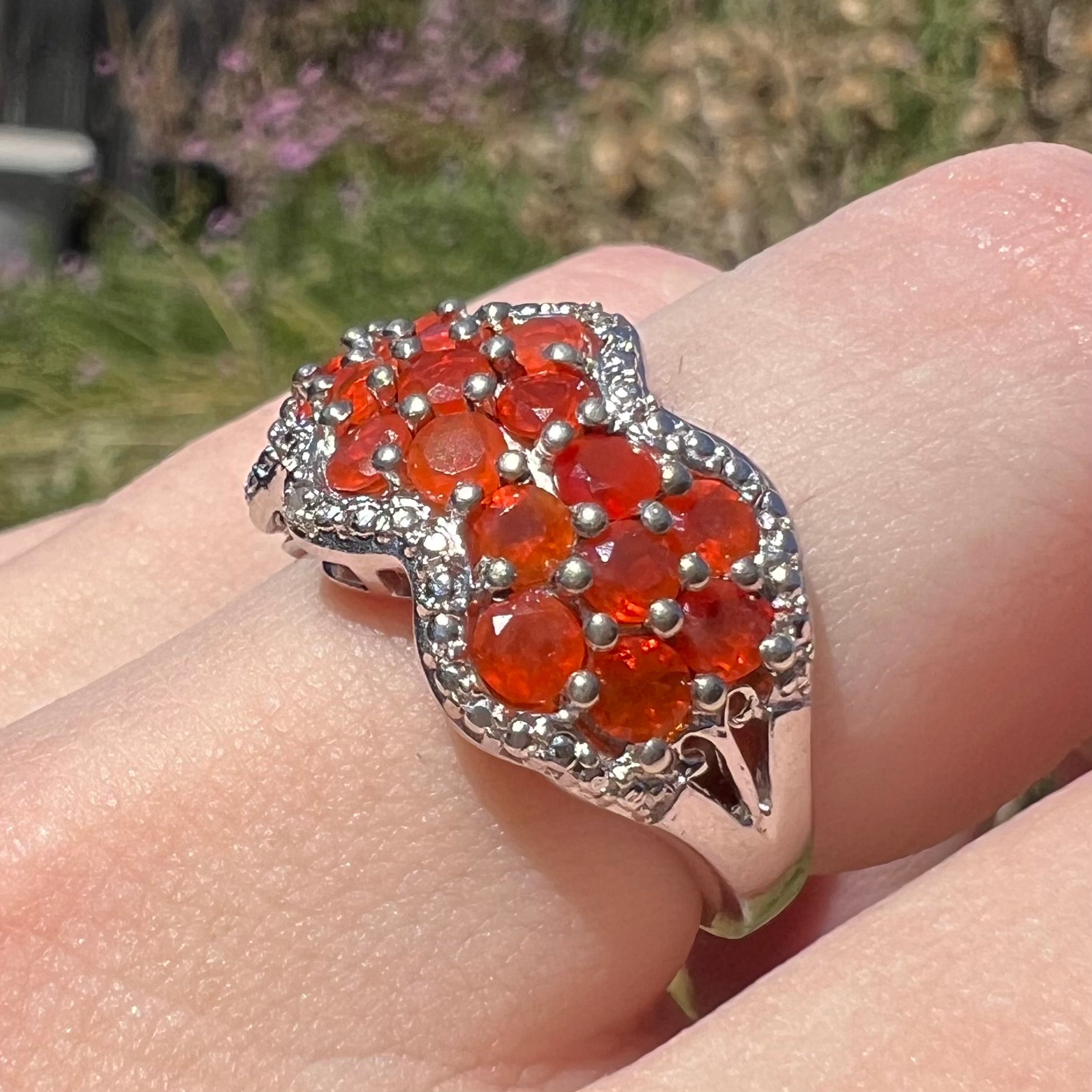 Angled macro close-up of a women's sterling silver fire opal and filigree design ring, worn on a finger in natural light.