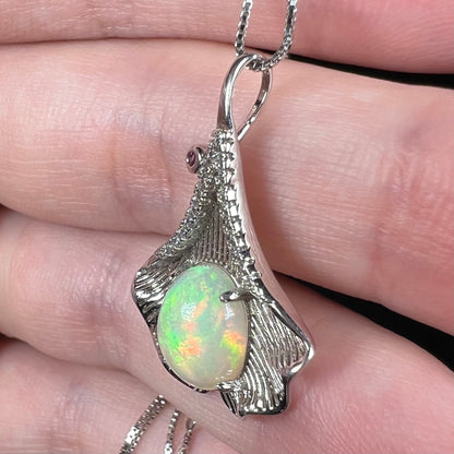 Side view of textured sterling silver ginko leaf pendant set with Ethiopian opal, held in hand
