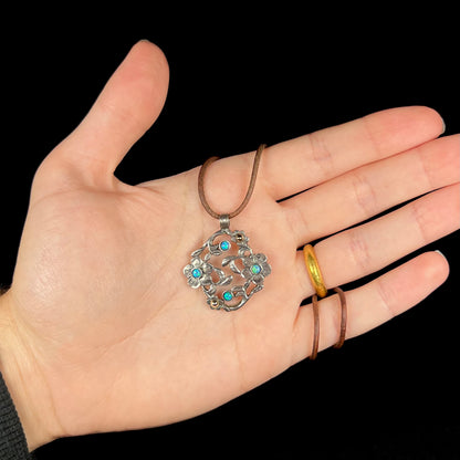 A two-tone sterling silver and 14k gold opal dogwood flower necklace on a brown cord in a hand against black background.