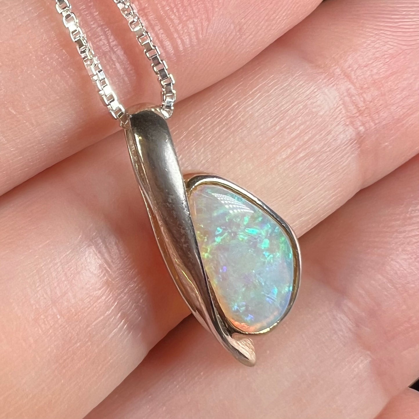 A green Australian crystal opal pendant in sterling silver shown close-up in a hand from an angle.