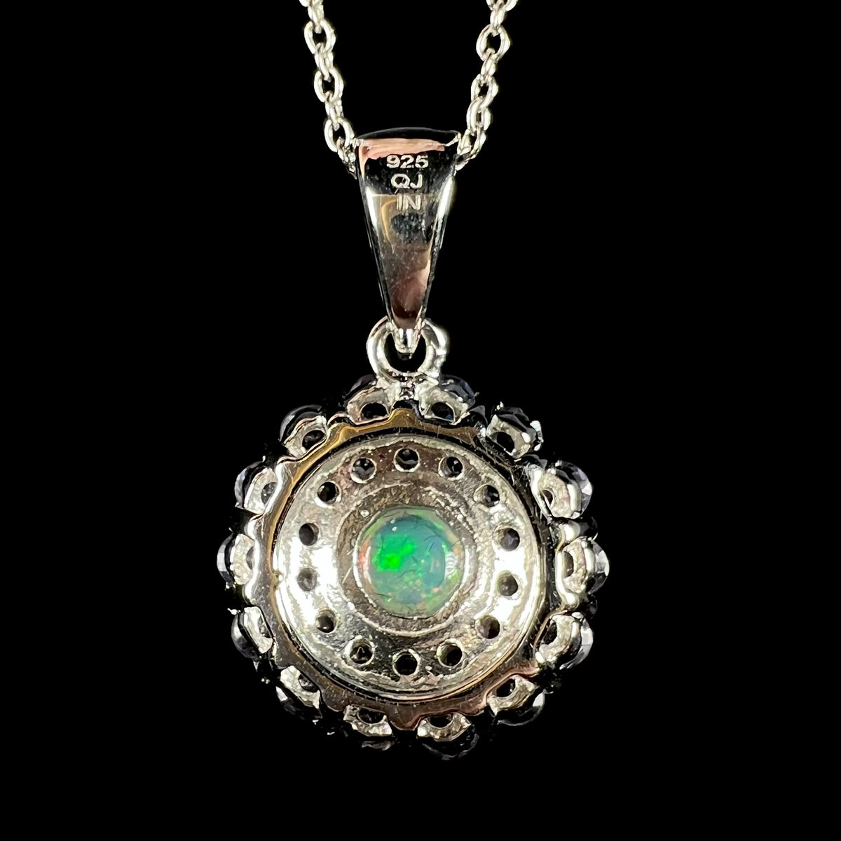 Back side of a round sterling silver pendant on a chain; the back of a green Ethiopian opal is visible, and the pendant's bail is stamped with the hallmarks "925", "QJ", and "IN".