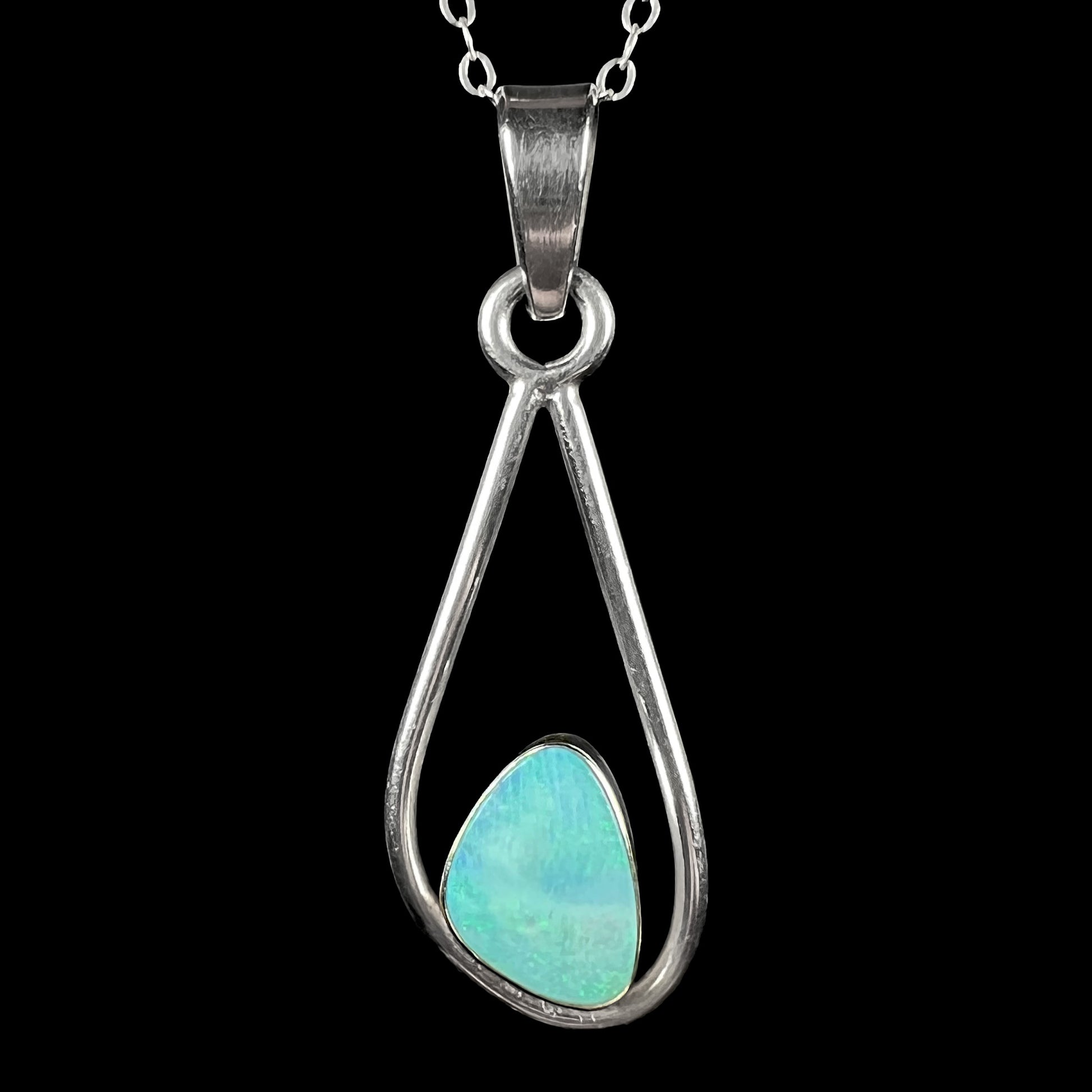 Macro shot of open Modernist-style sterling silver opal doublet necklace against black backdrop.  The opal is greenish blue under studio lights.