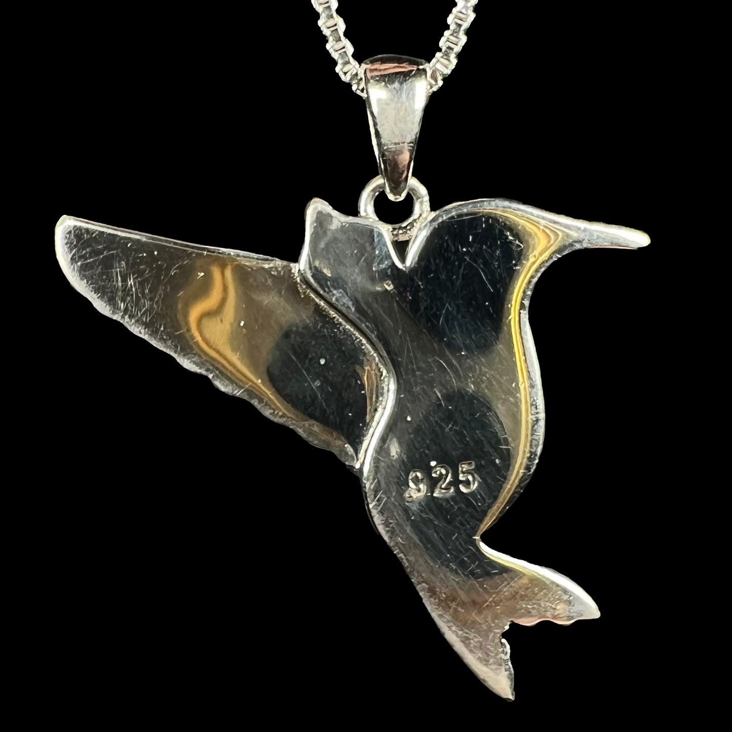 Back of a sterling silver hummingbird pendant on a silver chain, shown against a black background.