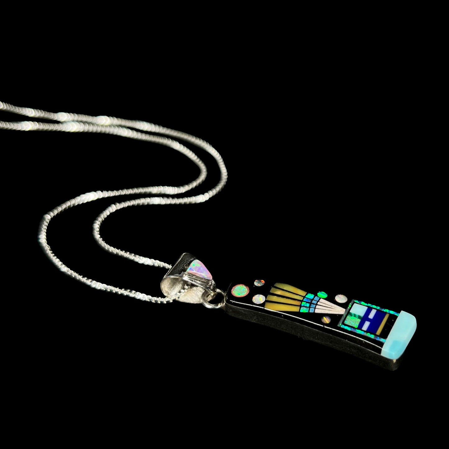 Sterling silver opal and onyx inlay necklace with kachina figure shown from angle laying on black background.