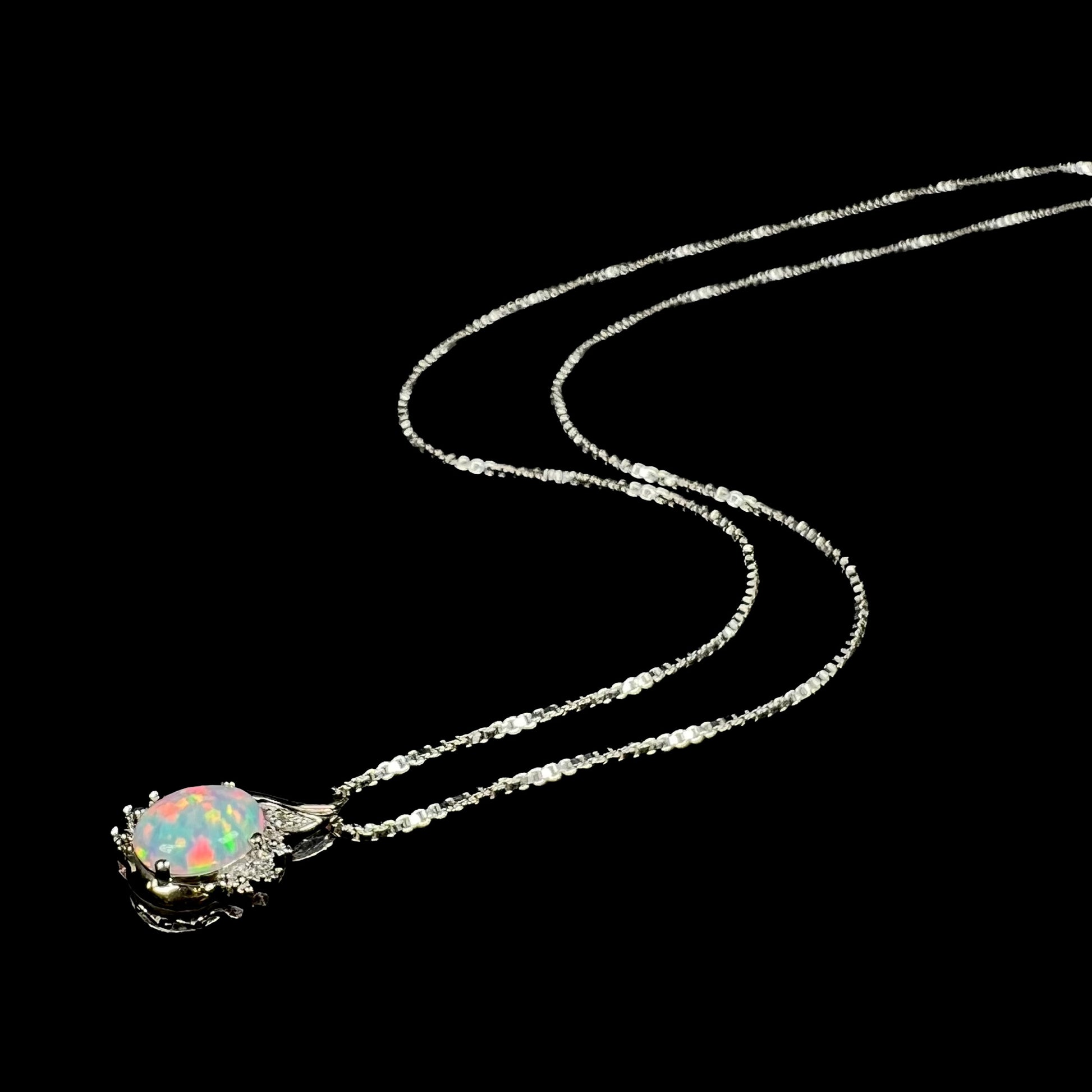 Angled view of a sterling silver lab-created opal and diamond necklace with its chain splayed out on a black background.