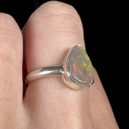 A sterling silver Lightning Ridge dark opal solitaire ring close-up on a hand, shown from an angle.  A subtle orange and green flash of color is present.