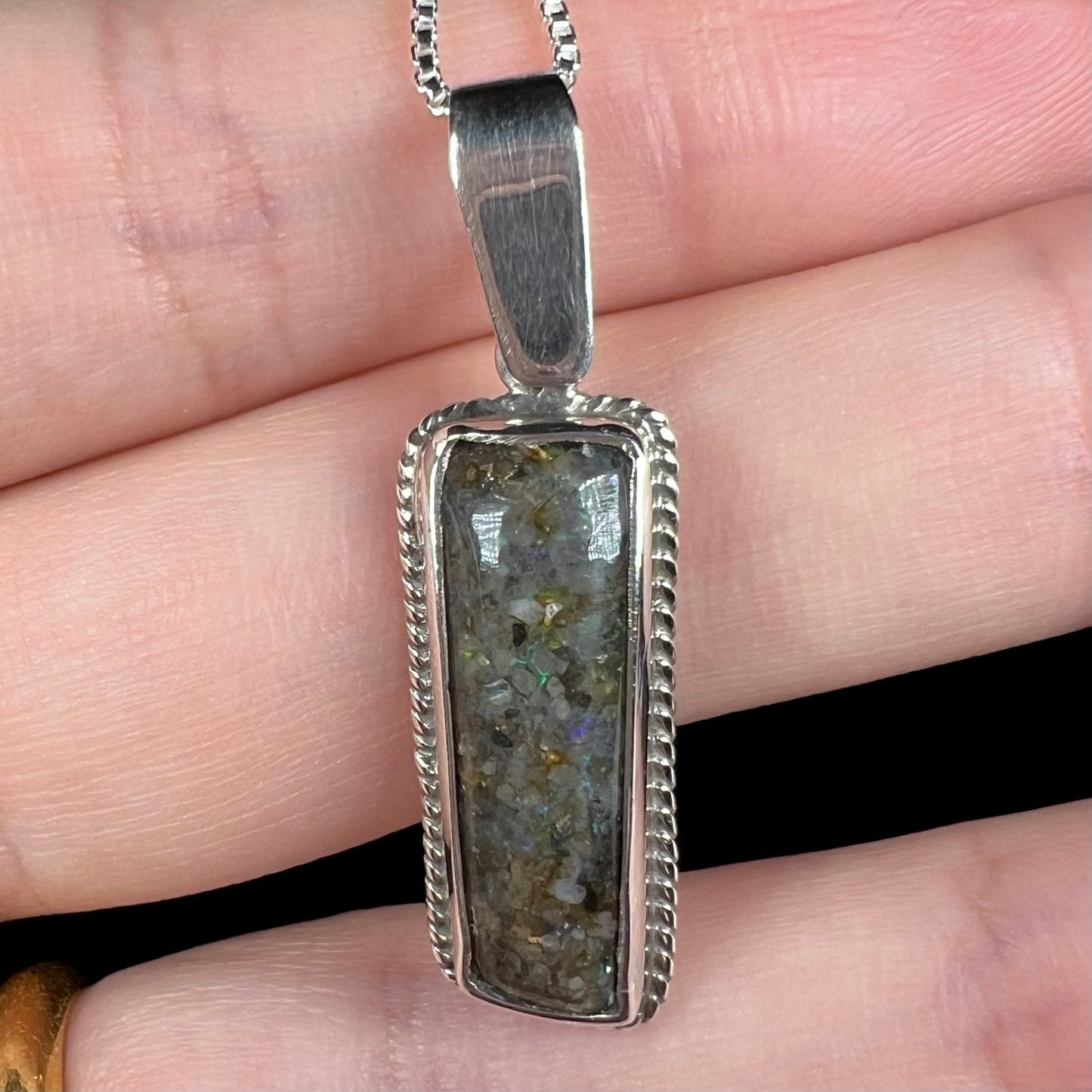 A Louisiana matrix opal pendant in sterling silver shown close-up in a hand.