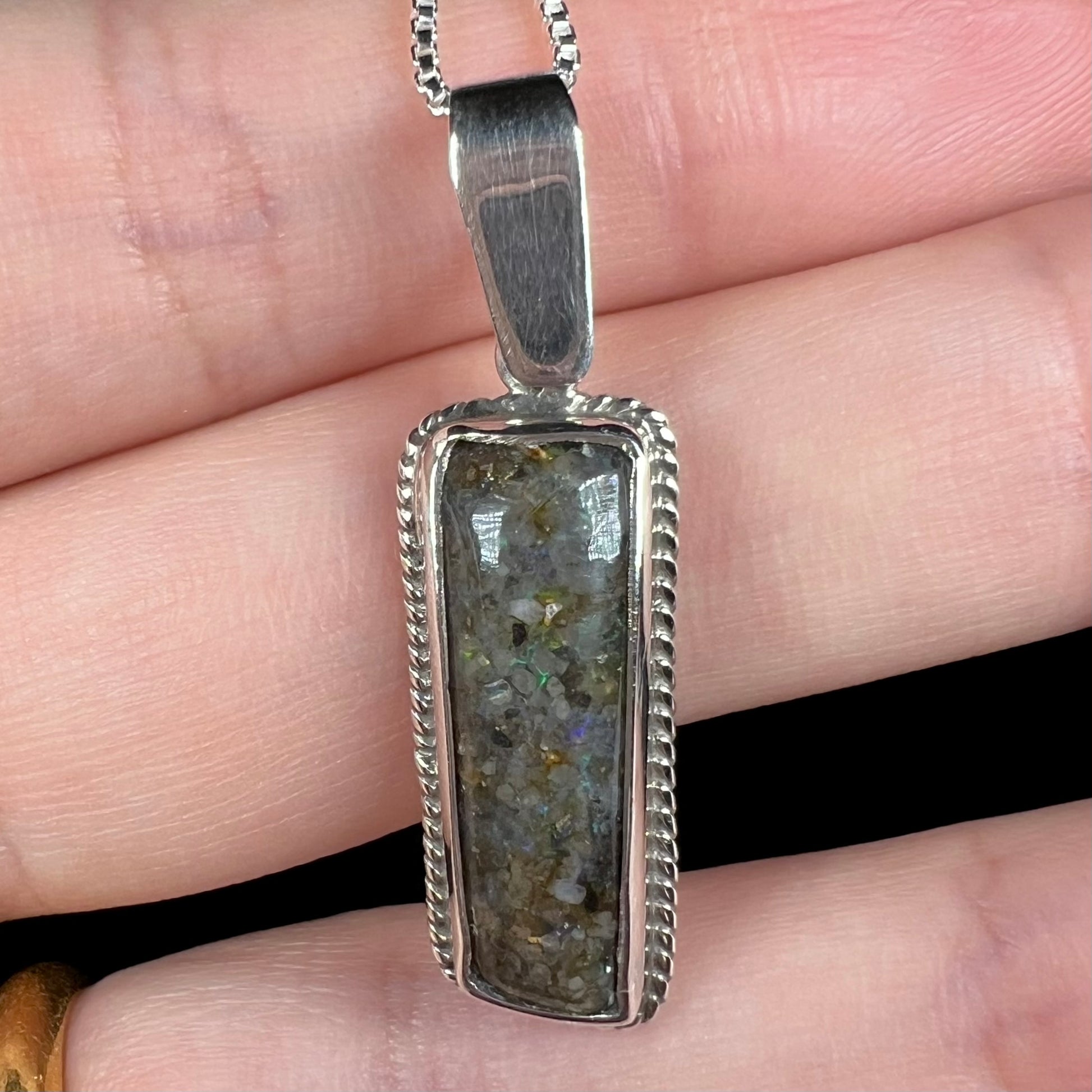 A Louisiana matrix opal pendant in sterling silver shown close-up in a hand.